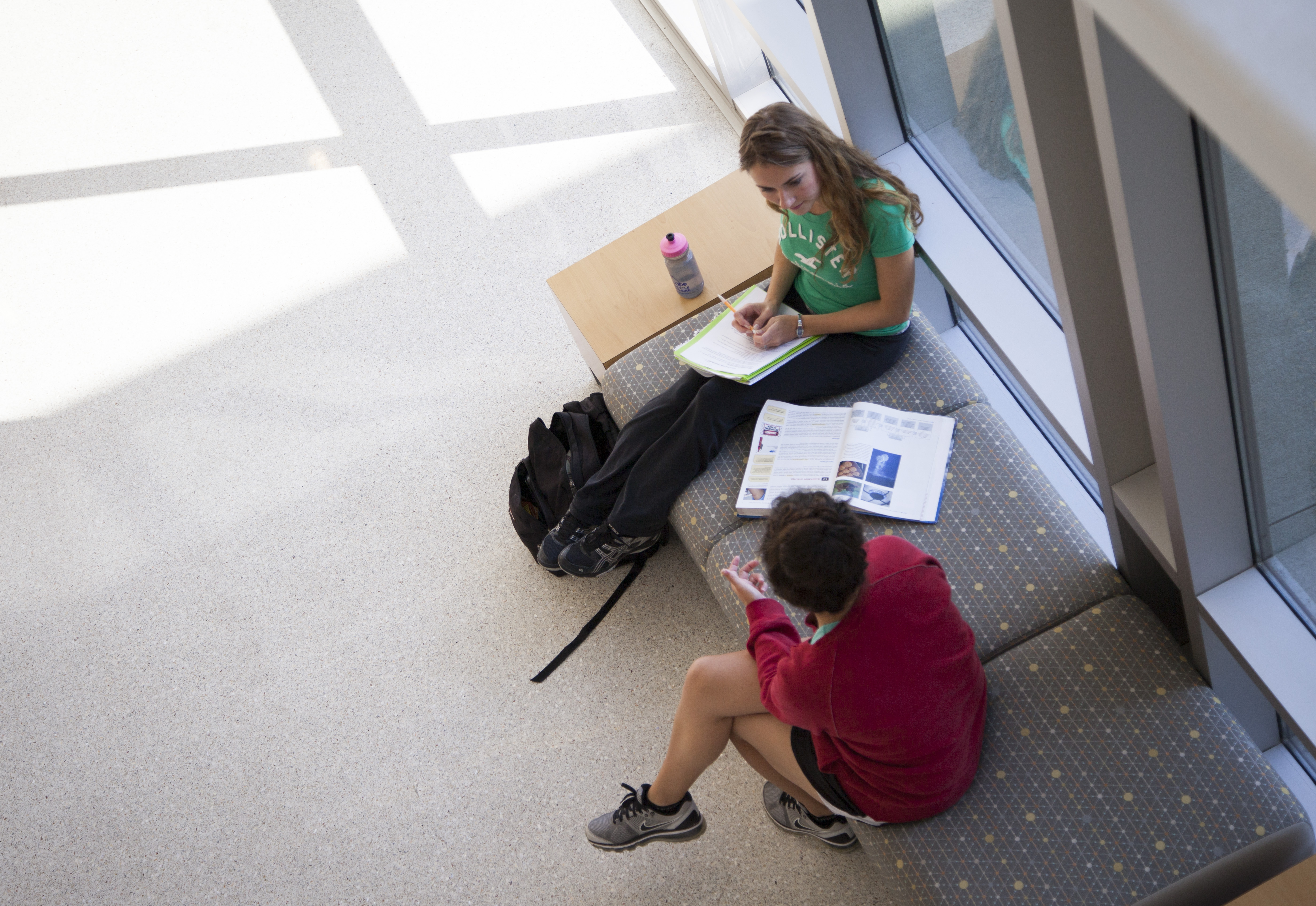 Two students studying on a bench with textbooks and notebooks
