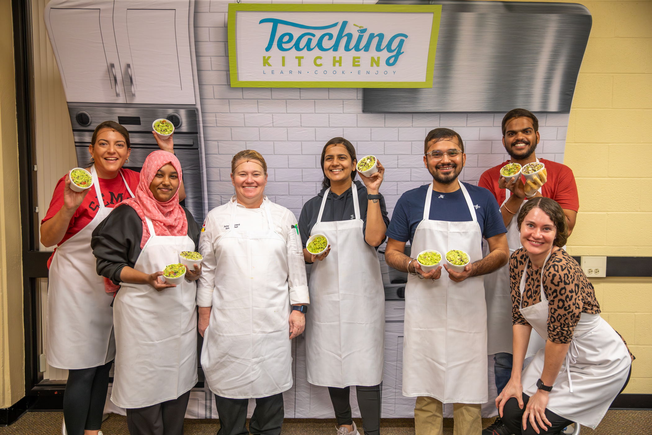 Students in a Teaching Kitchen class preparing their own guacamole, with fresh ingredients laid out on the counter and engaged in the cooking process.