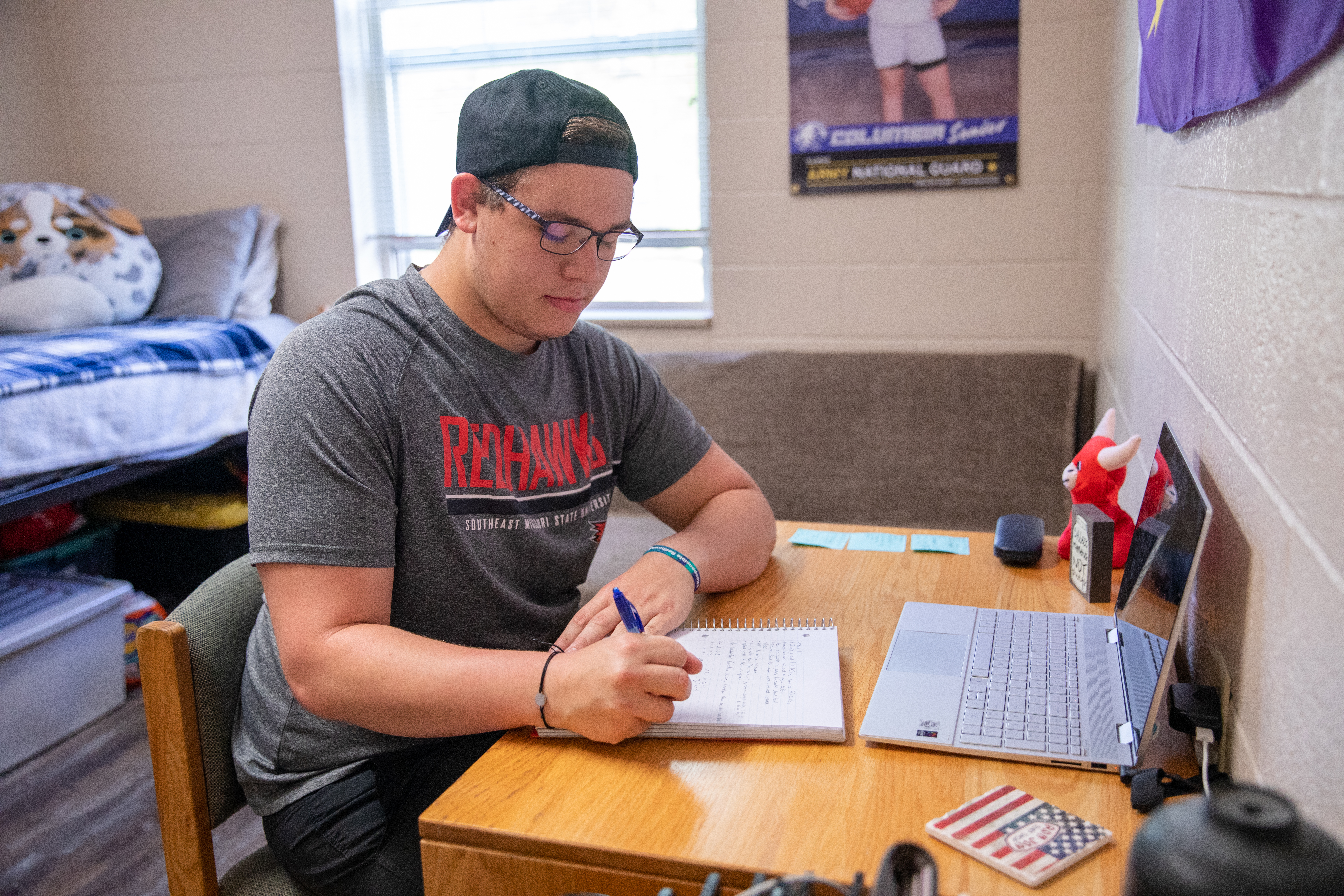Student sitting at desk in dorm room writing in notebook. 