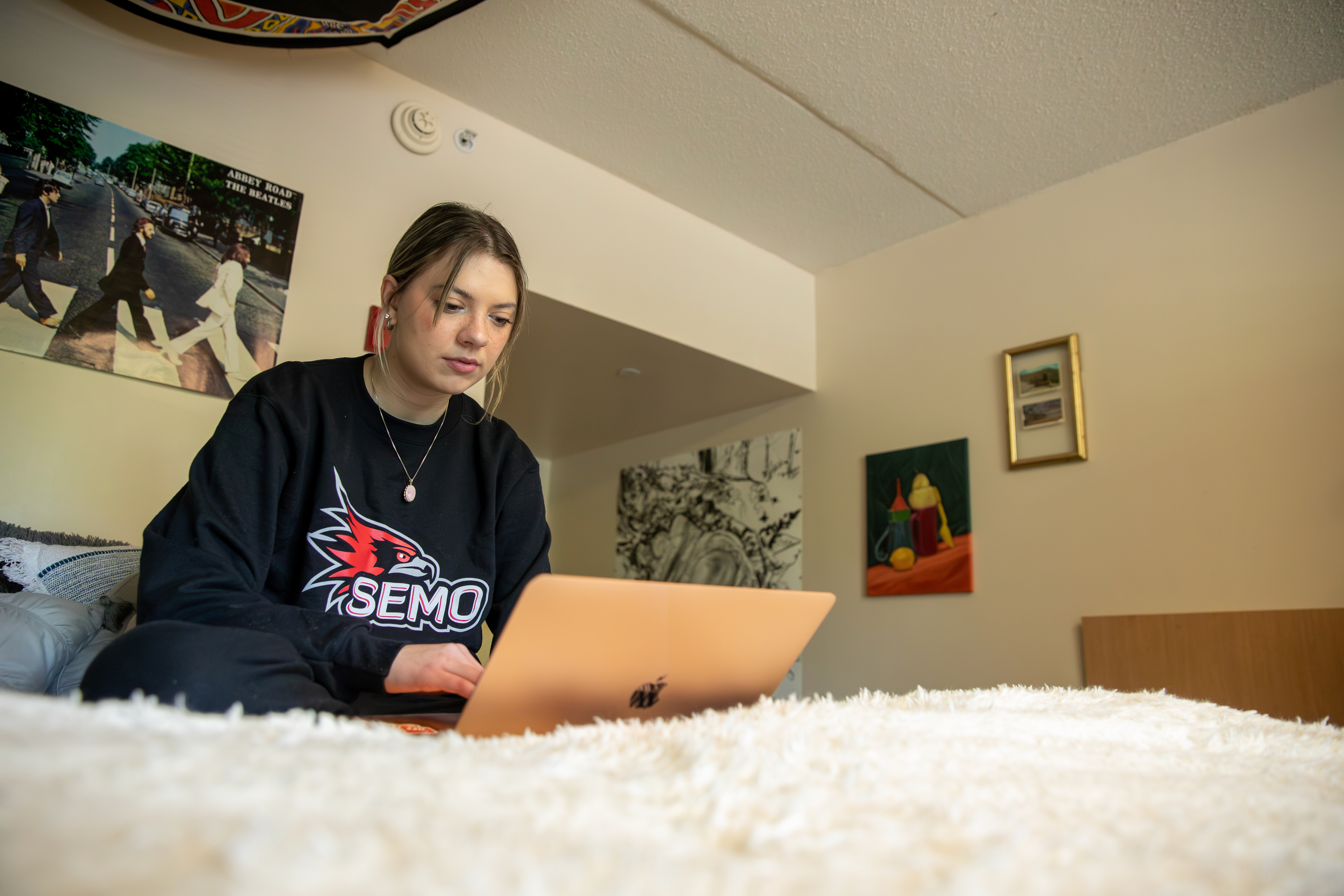 Student working on her laptop while sitting on her dorm bed