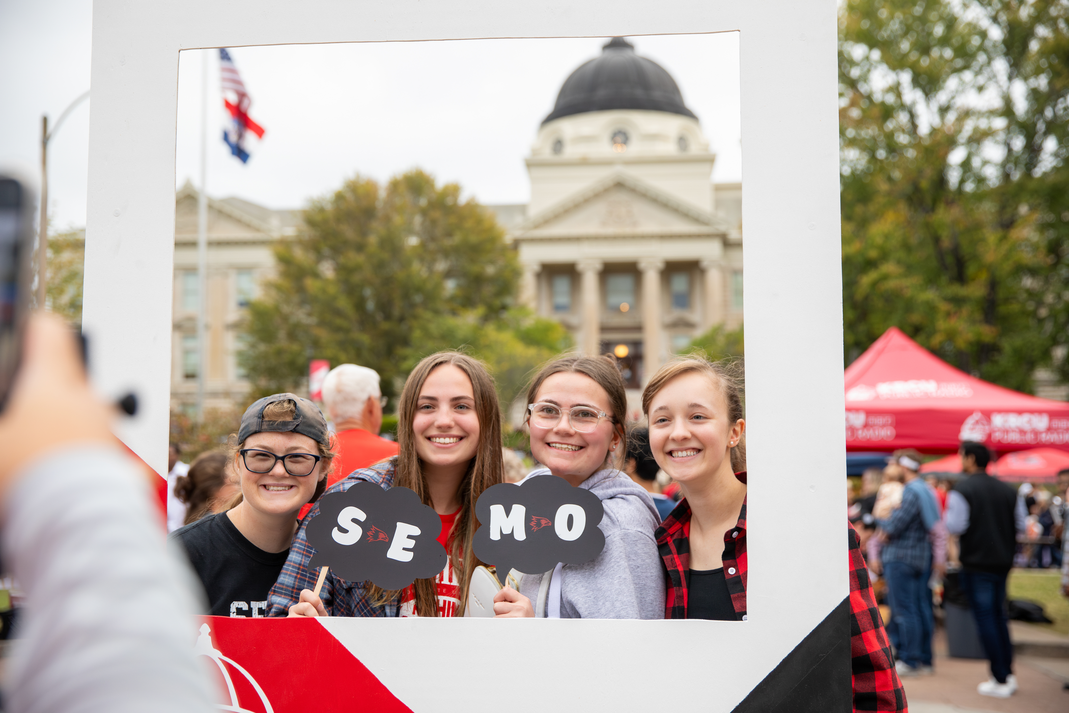 Four students standing and smiling in front of Academic Hall. 