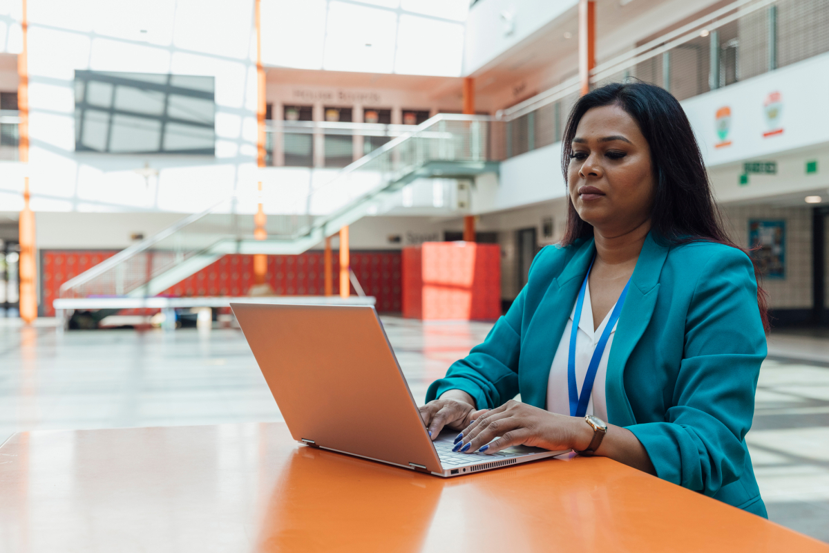 A school principal sitting at a table in a school looking at a laptop.