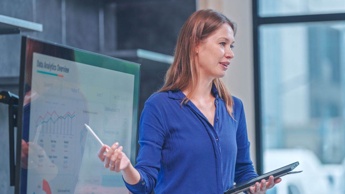 A data analyst presents some findings displayed on a large monitor.