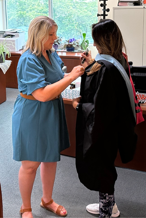 A professor helps Dr. Gupta put on her graduation robes.