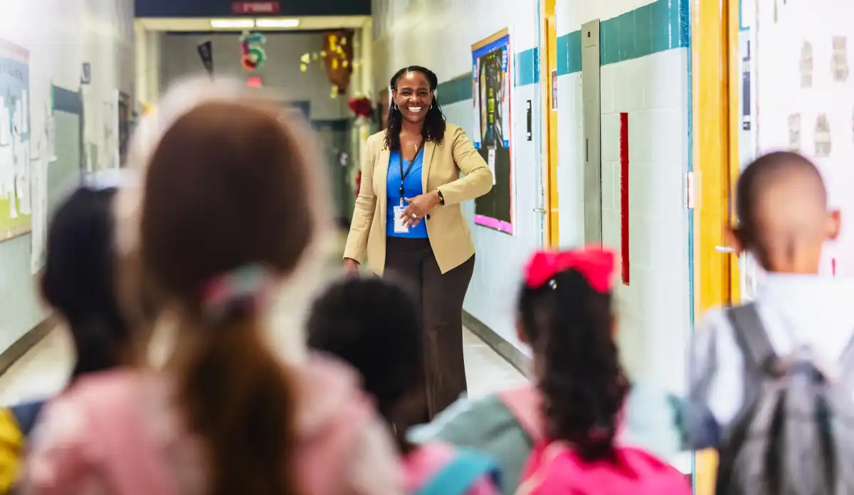 An elementary school principal greets students in the hallway. 