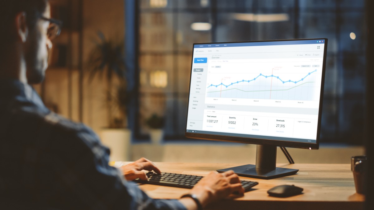 A financial analyst studies a graph on a laptop screen.