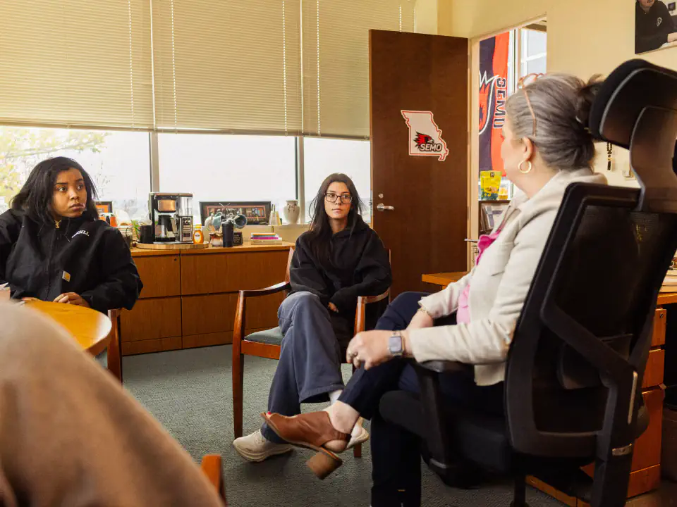 Students meet with a professor in her office, demonstrating how to interact with professors during office hours and ask for help.