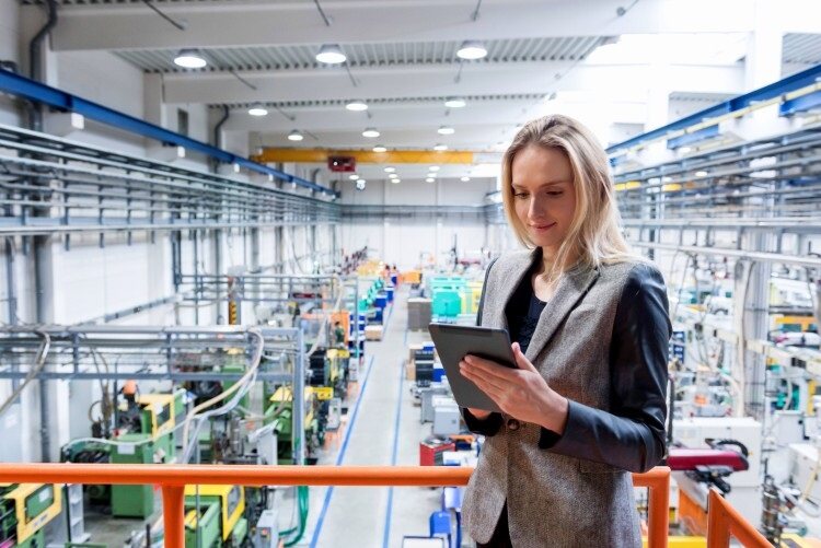 A production supervisor works on a tablet while overlooking the production floor.