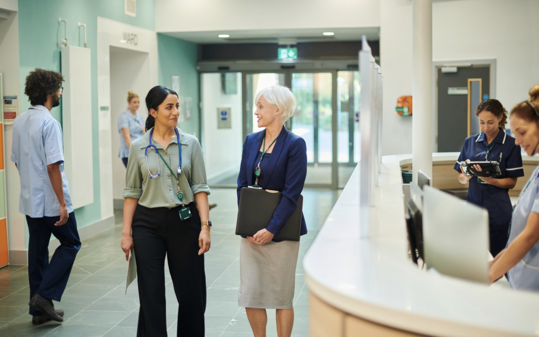 A healthcare manager talks with a physician in a hospital lobby.