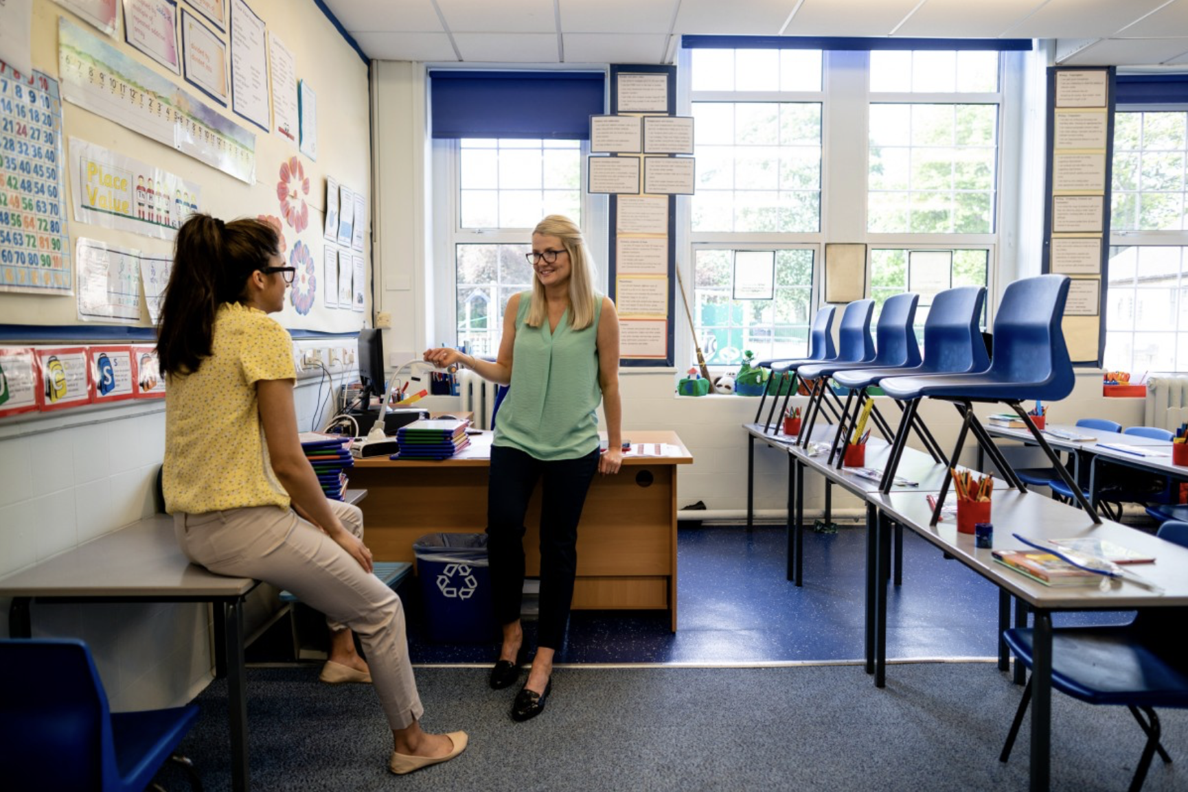 An instructional coordinator meets with a teacher in a classroom.