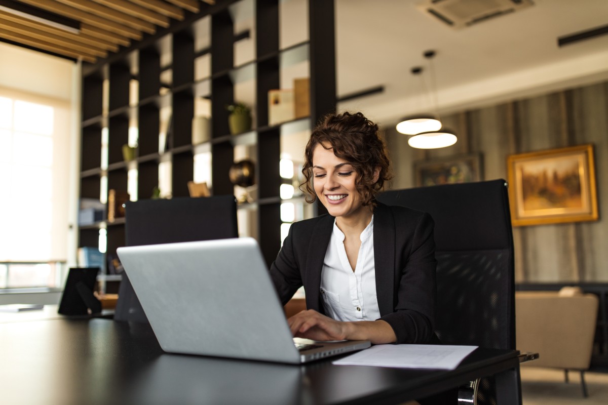A smiling social sciences professional works on a laptop in an office.