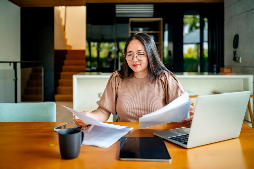 A professional sitting at a desk looking at papers and a laptop.