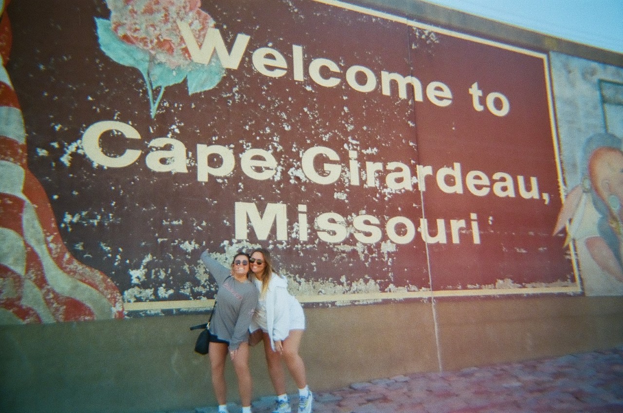 Taylor and another girl pose in front of a mural on the river wall that says Welcome to Cape Girardeau Missouri