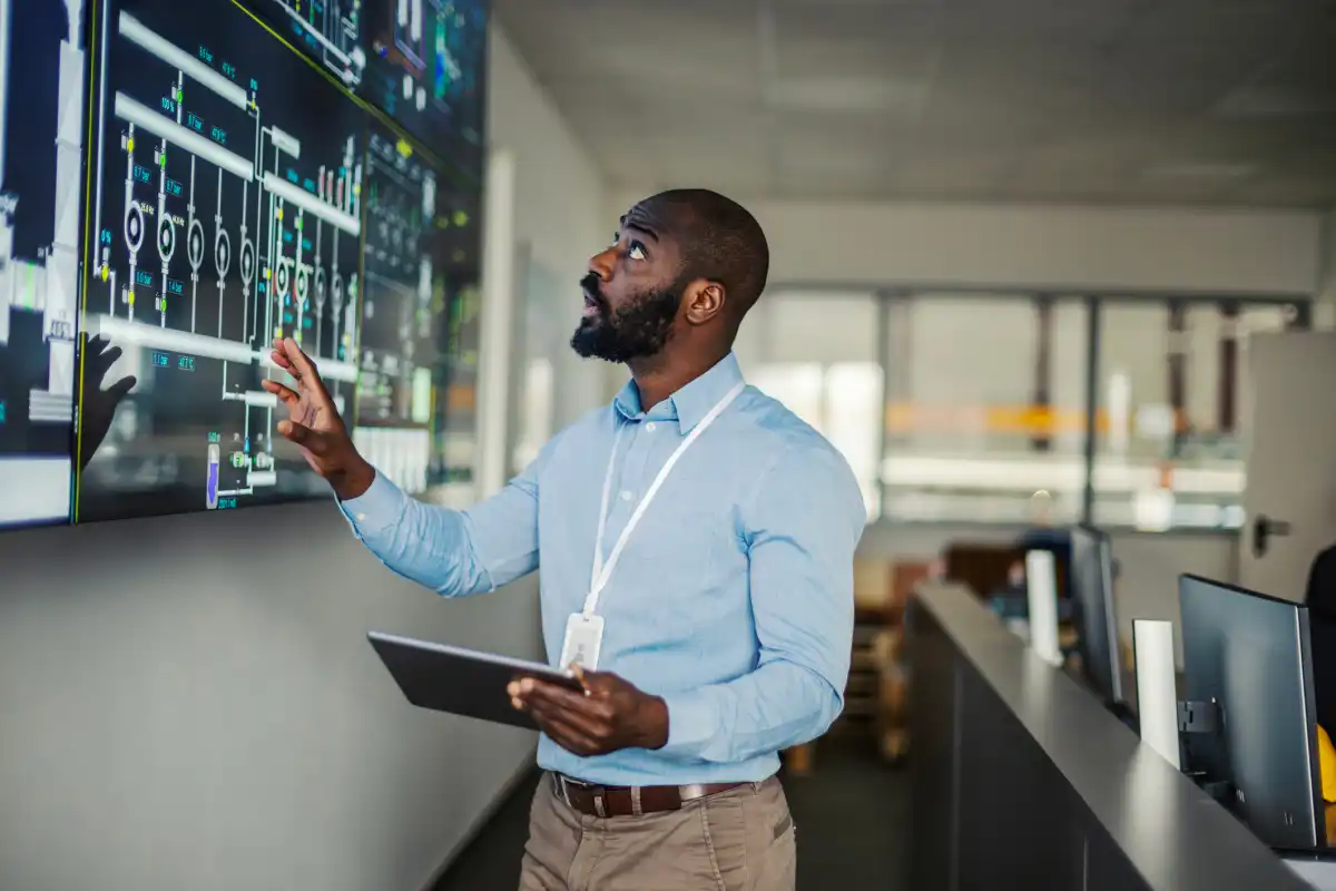 A technical program manager with a tablet reviews components of a complex process on a large screen.