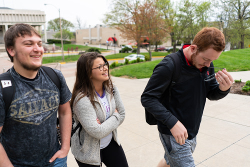 Three students walking together on campus, laughing.