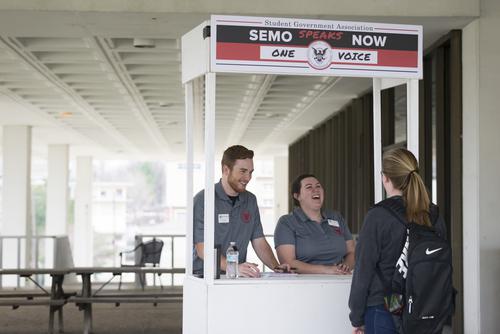Three Southeast students interact at a SEMO Speaks Now pop up stand on campus. 