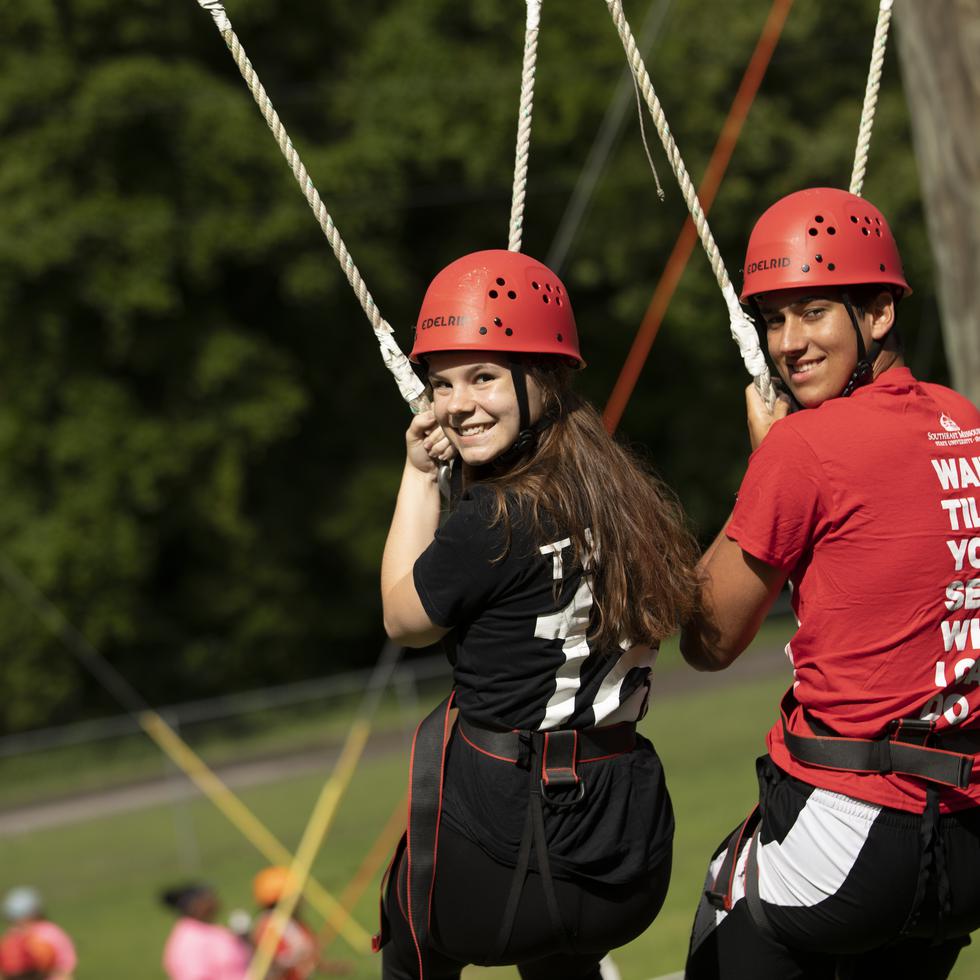 Two students attending Camp Redhawk pause for a picture while completing the Challenge Course.  