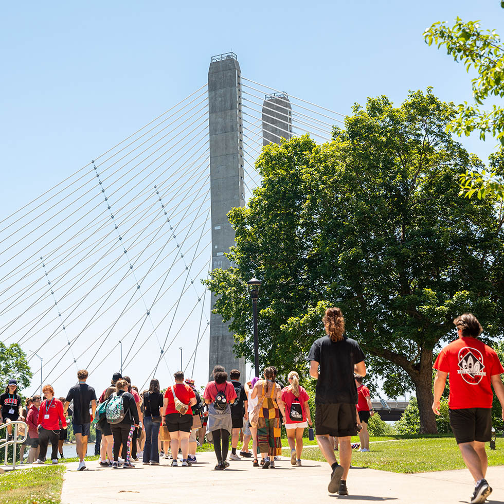 camp redhawk students tour the River Campus grounds - the mississippi river bridge rises up in the background against a clear blue sky