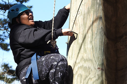 a student in safety gear climbs a pole on an obstacle course