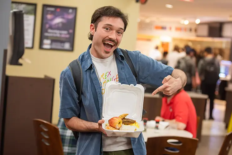 a SEMO student attending the late night breakfast happily gestures at his container of food