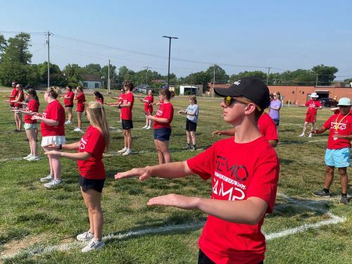 a group of kids stand on a field improvising holding their instruments in band formation.
