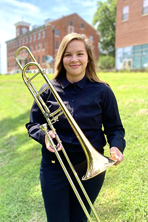 portrait of Ashleigh holding her trombone on the River Campus lawn