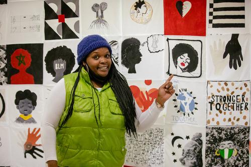 A student attending the Bridges event points to their artwork in the Collaborative Quilt Story Project.  