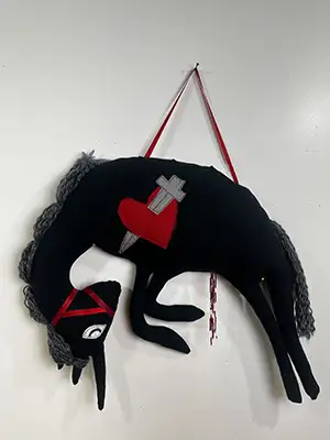 a fiber sculpture featuring a black unicorn wearing a red bridle, on it's side is a red heart with a sword through it