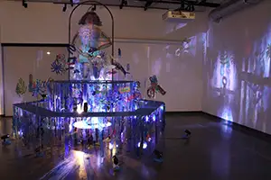 an art exhibit featuring pieces of transparent material arranged in fountain-like tiers. Has blue lights and casts shadows on the gallery wall