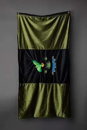 a piece of fiber art - it is a flag with two dark olive green fields on each end, top and bottom, in the middle is a black field with a tropical parrot and a body of water and grass