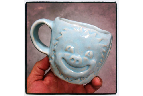 A light blue ceramic mug with a face with spiky hair engraved on it. 
