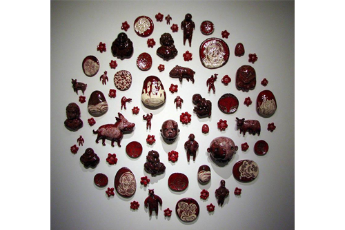 A display of ceramic pieces hanging on a wall. The pieces include heads that vary in color from red to brown. There are also flowers and a cow hanging on the wall. 