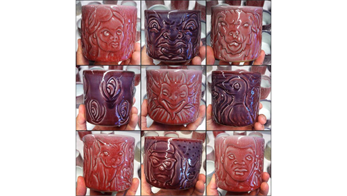 A grid of 9 ceramic mugs that range in color from red to burgundy. They each have engravings including a devil face, a bird, a cat, and human faces. 