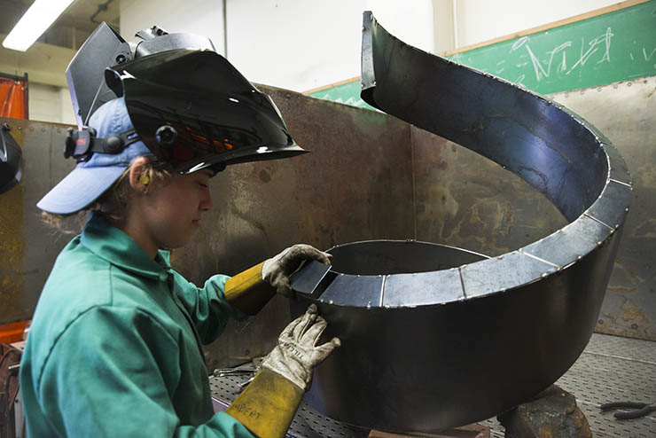 a sculpture student works in the studio to put her metal sculpture together
