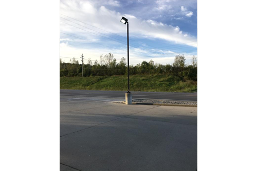 A light post with a blue, cloudy sky with grass and trees behind the pole 