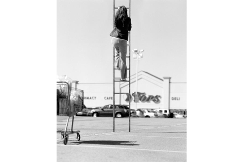 A woman climbing a ladder with a grocery store in the background 