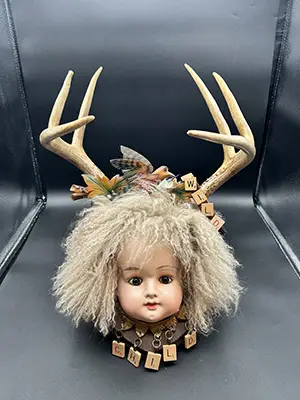 a sculpture featuring a doll's head and antlers