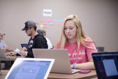 A mass media student works on a laptop during class.