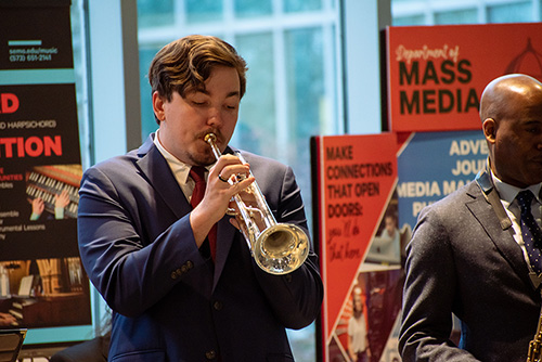    Student plays the trumpet while performing outside the hall in River Campus.
