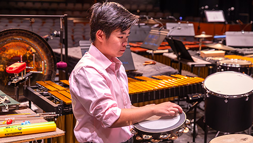 A student touches the rim of a drum during a percussion practice.