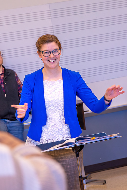 During trumpet ensemble, a woman in a blue coat is conducting the session.