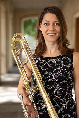 young woman with brown hair posed with her instrument in front of an architectural background