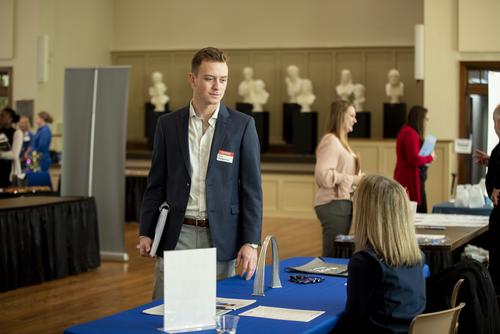A student wearing a name tag speaks with a hiring professional at a career fair.