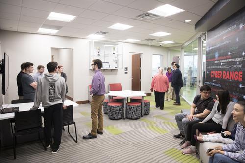 Numerous students talk while sitting and standing around the Cyber Range.