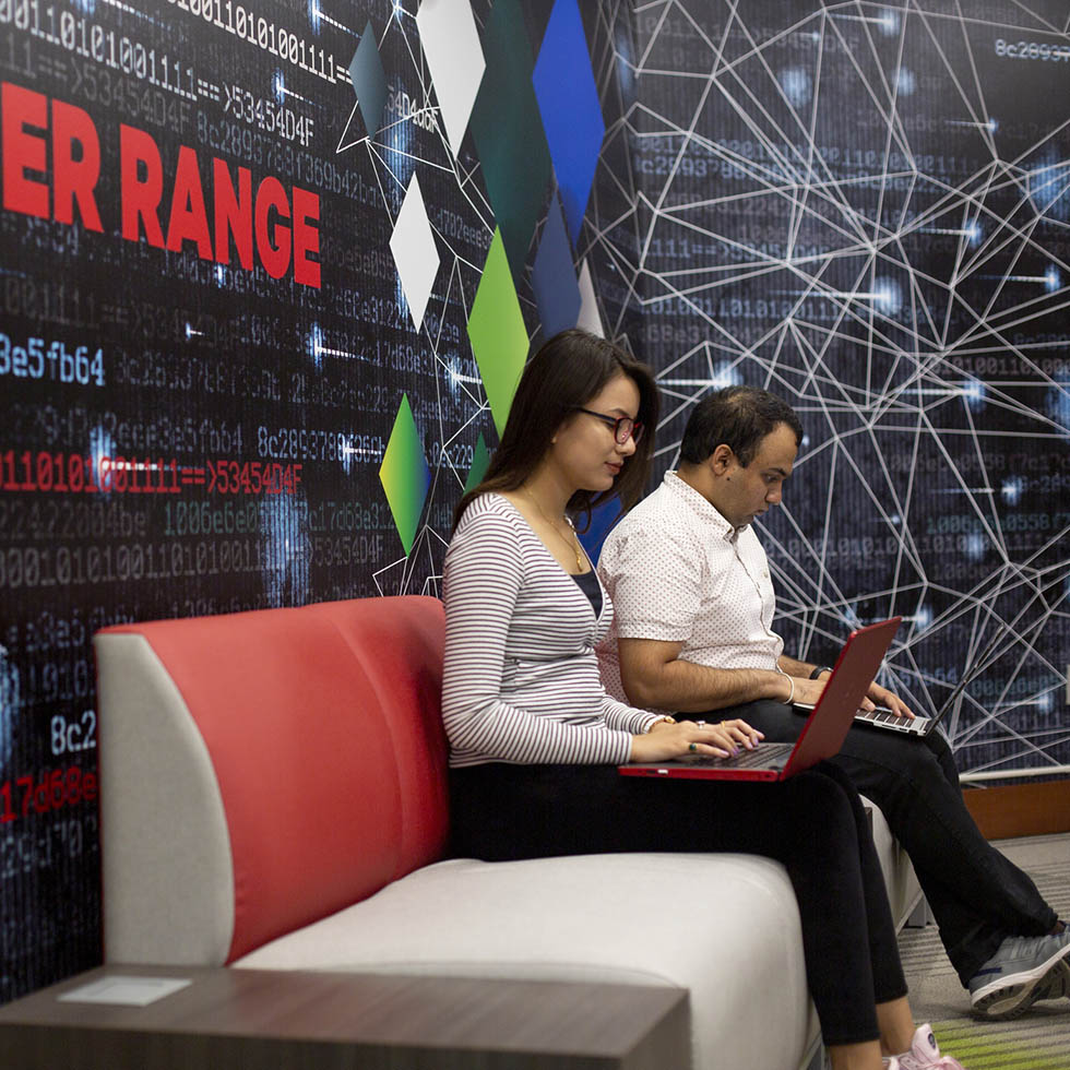two southeast cybersecurity degree students sit in the cyber range and work on their laptops
