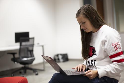 A business student works on a laptop in a Dempster Hall classroom. 