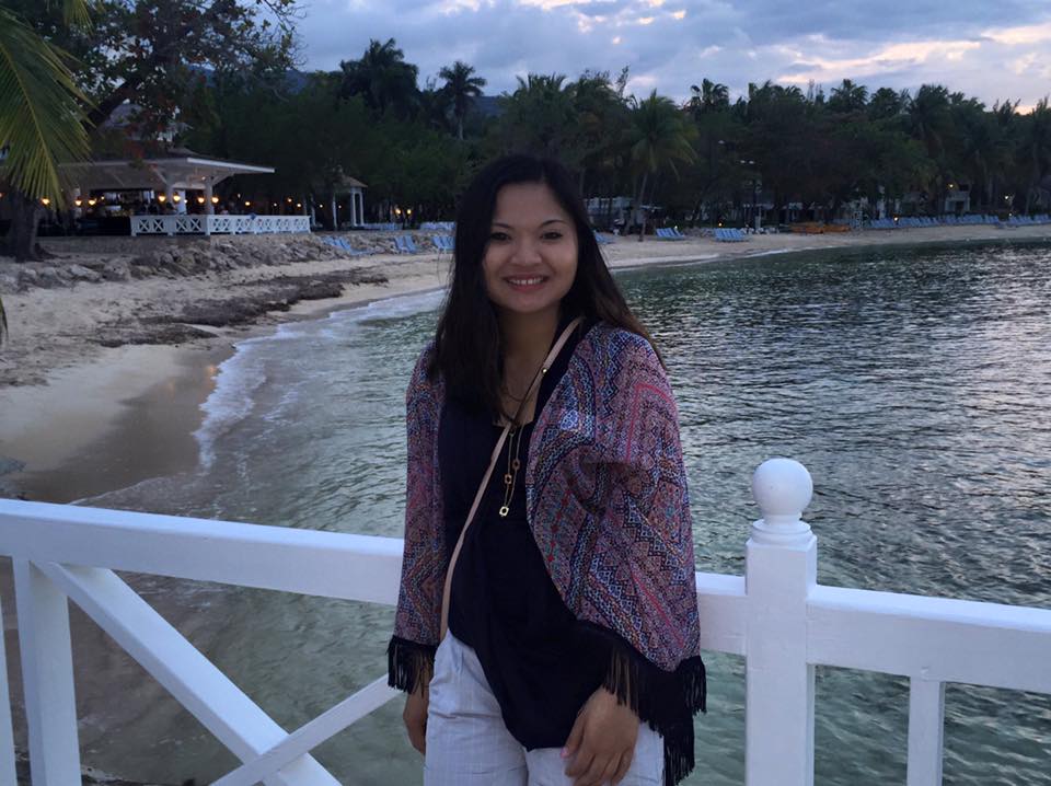 Thu Nguyen stands on a bridge with a white railing at a beach.