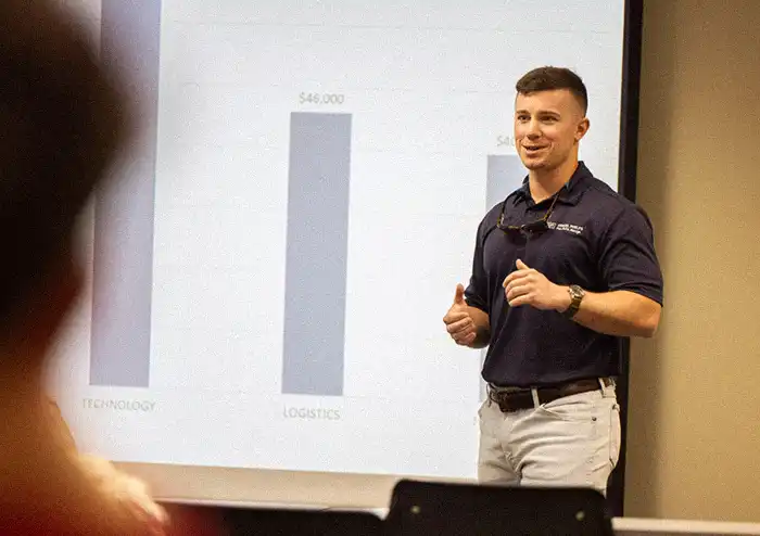 Male student in the marketing degree program giving a professional presentation, using a PowerPoint with graphs and data.
