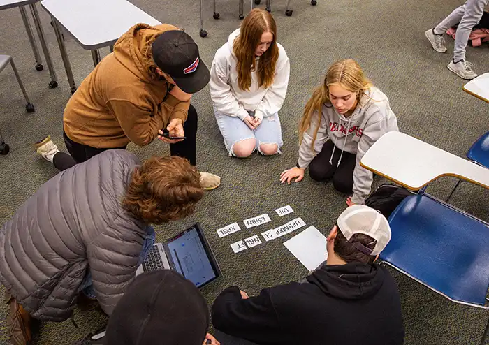 Group of students in the marketing degree program, in class, sitting on the floor, solving a puzzle assignment.