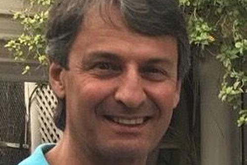 Karim Mansouri, smiles, standing outside wearing a blue shirt.